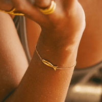 Bracelet Poisson en plaqué or, porté au poignet avec bagues